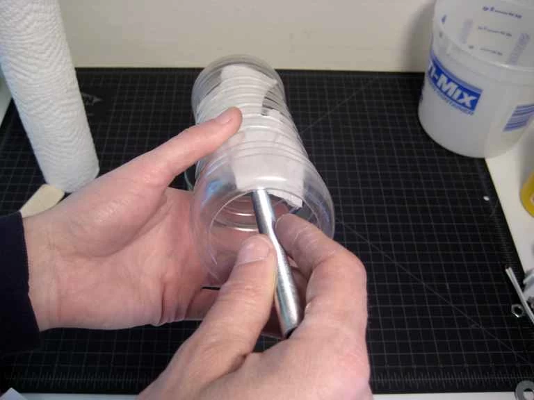 有人用一根棍子和一張紙巾將凡士林塗抹在塑膠瓶內壁上。