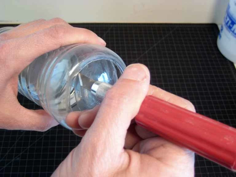 一個人用鋒利的刀子切掉塑膠瓶的底部。