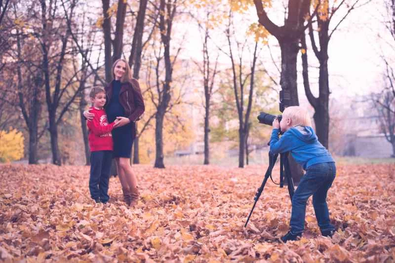 一個金髮小男孩,手裡拿著一台架在三腳架上的單眼相機。