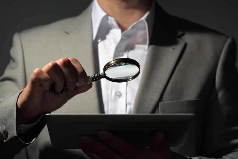 一名身穿灰色西裝的男子正在用放大鏡查看平板電腦。