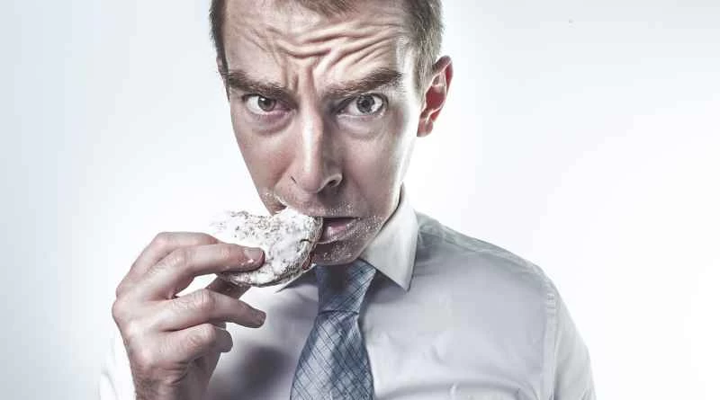 一個穿著西裝的男人正在吃餅乾，一臉嫌棄。