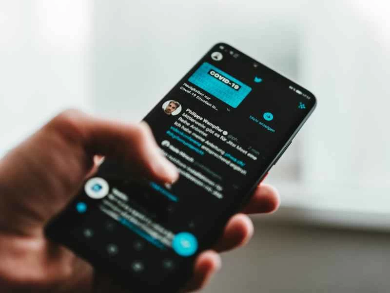 一個人拿著手機,在深色模式下使用 Twitter,瀏覽有關 COVID-19 的推文。
