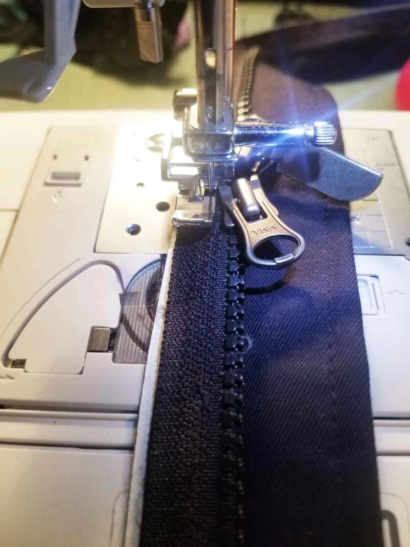 一個人正在用縫紉機縫製冬裝外套替換拉鍊。