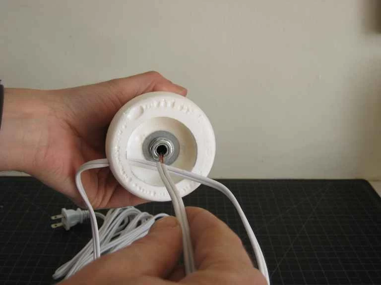 一個人正在將電源線穿入自製塑膠燈的底座中。