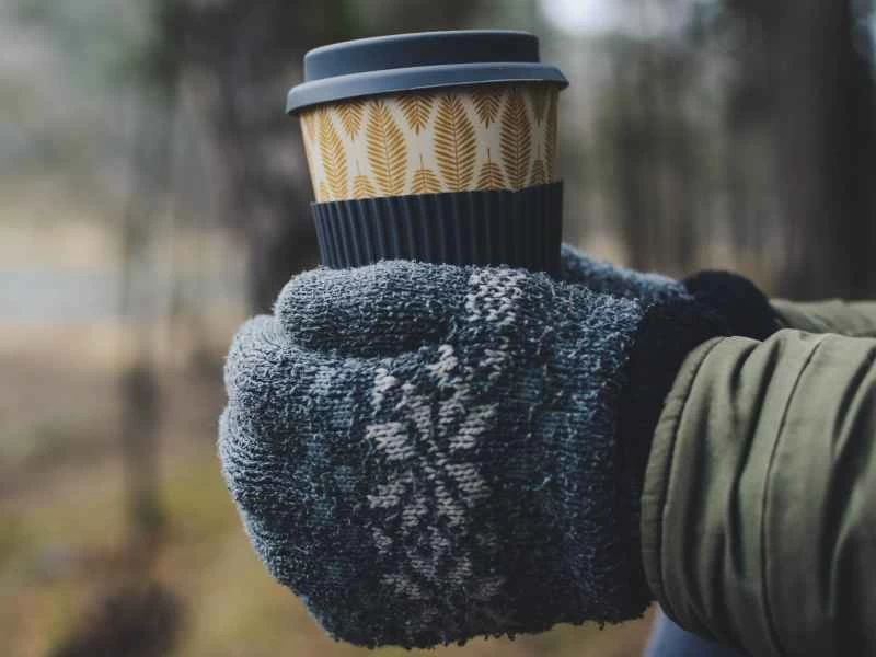 戴著針織手套的手拿著一次性杯子在戶外。