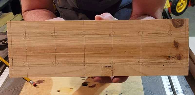 一名男子拿著一塊木板放在工作台上，向鏡頭展示。木板上畫著一個雞蛋托架的圖案，是一個2x6的方格。